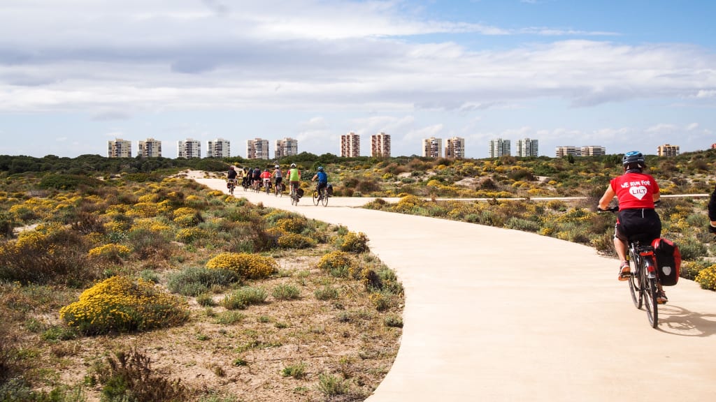 Ciclista su pista ciclabile lungo il fiume Turia con skyline moderno di Valencia sullo sfondo, itinerario urbano in bici in Spagna